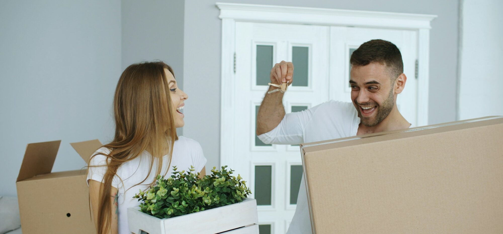 Una pareja sonriendo con las llaves de su nueva casa, rodeada de cajas de mudanza